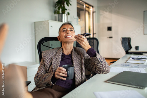 Smiling businesswoman using voice assistant in modern office