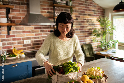 Smiling woman unpacking fresh groceries in home kitchen