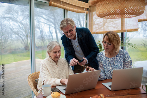 Canvas Print Three mature adults collaborating on laptops in a bright home conservatory