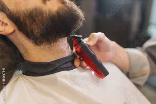 Φωτογραφία Barber trimming beard of male client with electric clipper in barbershop
