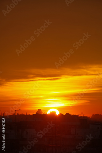 Golden Sunrise Over City Skyline With Silhouetted Buildings and Calm Orange Sky At Dusk Tonight