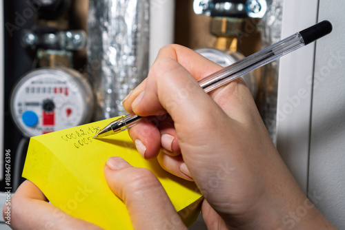 Woman reading the water meter in the apartment building, counter for distribution domestic water. Woman recording meter readings, water meters of cold and hot water, consumption in apartment. Billing.