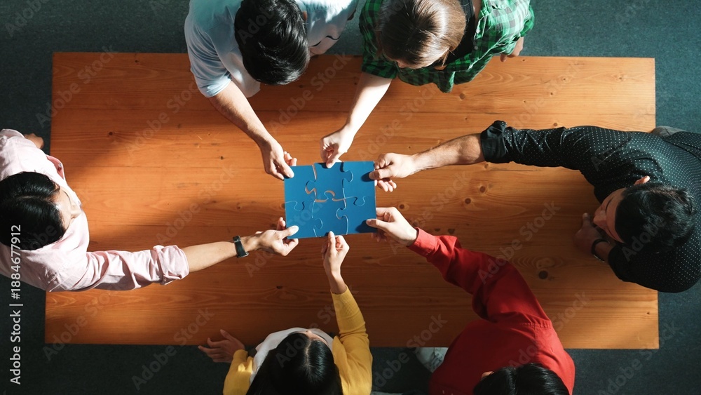 Obraz premium Top down view of skilled business people assemble blue jigsaw puzzle on meeting table. Group of diverse team working together to solve the puzzle. Represented togetherness, cooperative. Convocation.