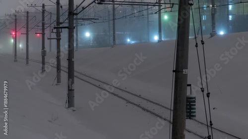 Railway tracks covered in snow under a foggy sky with illuminated signals and Trains. Time-lapse.