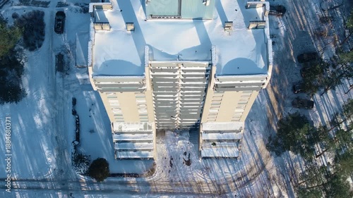 Drone ascending over a modern apartment building in a snowy urban neighborhood on a sunny winter day