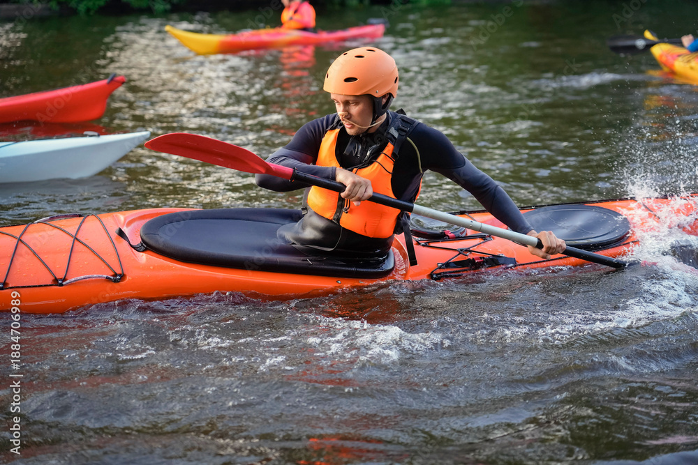 Fototapeta premium Participants paddle on a calm river at sunset, showcasing vibrant kayaks and a peaceful atmosphere. The water reflects the warm colors of dusk as outdoor enthusiasts engage in the sport