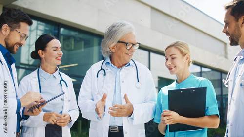 Wallpaper Mural Group of Caucasian doctors gathered outside clinic. Male specialist explaining case details. Female interns reacting with smiles. Senior physician listening during training session outdoors. Teamwork. Torontodigital.ca