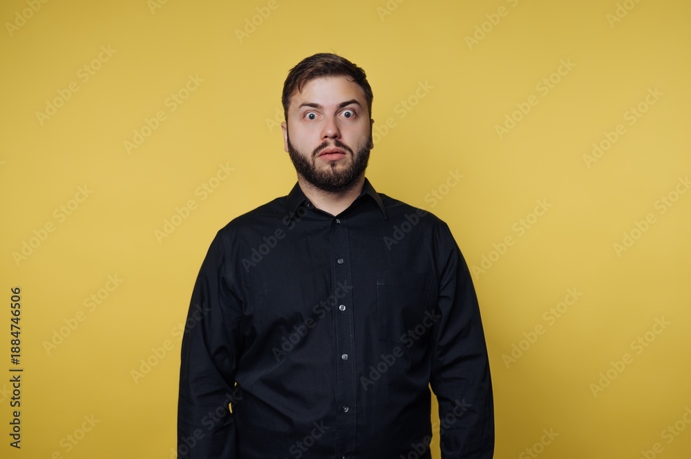 Fototapeta premium Man in black shirt with surprised expression on yellow background.