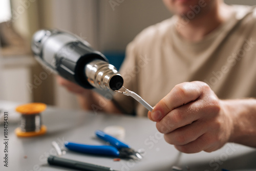 Slika na platnu Close-up of person hands working on damaged electronic cable, applying heat with heat gun to shrink tubing or solder connecting wires, signifying diligent repair work and technical expertise