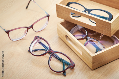 Variety of stylish eyeglasses in wooden organizer boxes on a wooden table