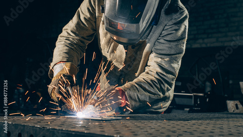 Photos A professional metal worker welds steel in an industrial workshop, wearing protective gear as bright sparks fly from the welding process