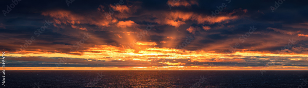 Fototapeta premium Sunrise over ocean horizon with dramatic clouds and warm glowing light reflecting on calm water surface