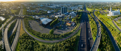 Aerial view of Manukau, Auckland, New Zealand, showing the city skyline, highway traffic, commercial buildings, and the Auckland New Zealand Temple. Illustrates urban planning and transportation.
