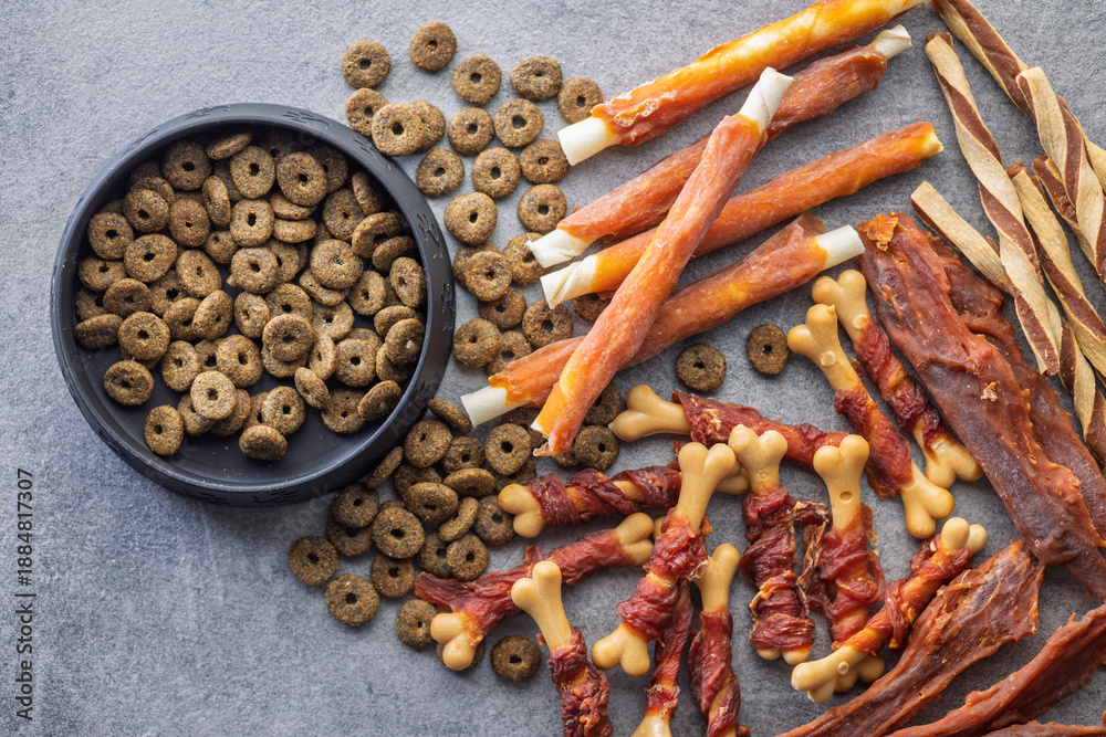 Naklejka premium Dog food. Snack sticks for dogs and dry kibble food on gray table. Top view.