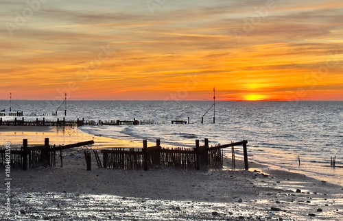 A rich orange sunset over Hunstanton beach with old wooden groynes in the foreground, Norfolk, England, UK. 
