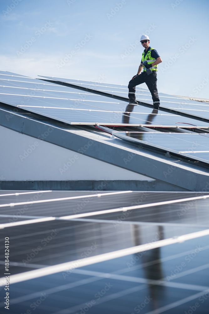 Fototapeta premium Technician installing solar panels on factory roof for green energy. A skilled technician in safety gear is working on a solar panel installation on rooftop.