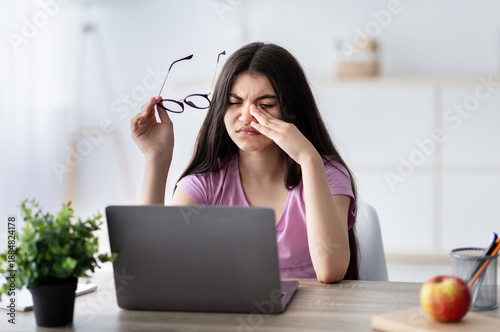 Schilderij op canvas Indian teenage girl feeling tired, rubbing irritated eyes, sitting at desk with laptop, exhausted from online studies