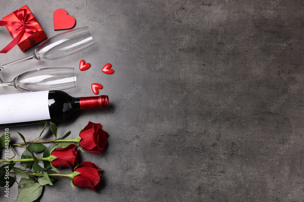 Fototapeta premium Beautiful roses, wine with glasses, gift and decorative hearts on grey background, flat lay. Space for text
