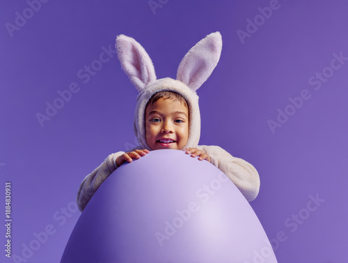 Adorable child dressed in a soft bunny costume holding a large purple egg with a joyful expression on a matching solid background