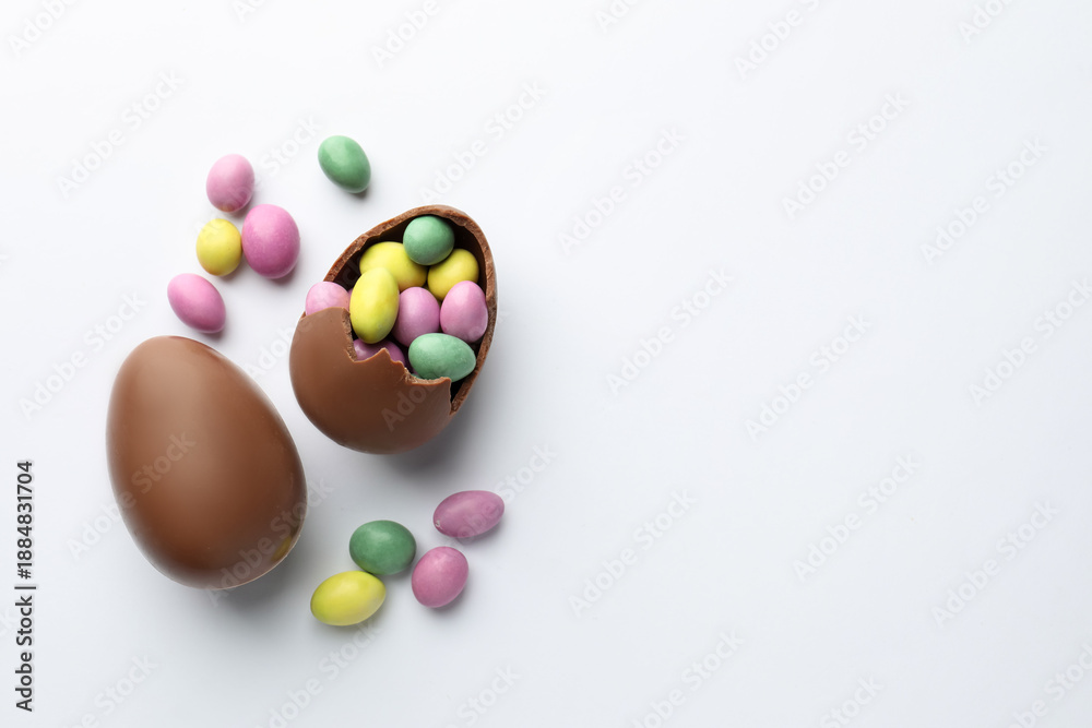 Obraz premium Chocolate Easter eggs and candies on white background, flat lay. Space for text