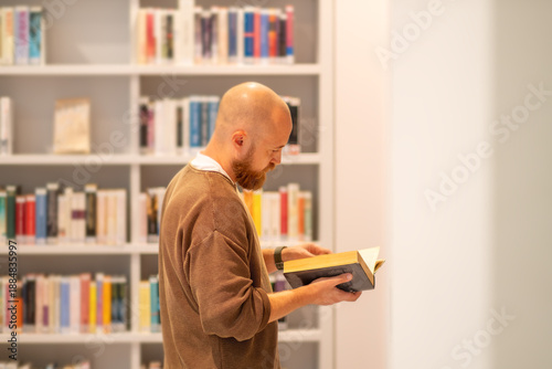 Smart man choosing book from bookshelf. Textbook resources in library for educational research and reading