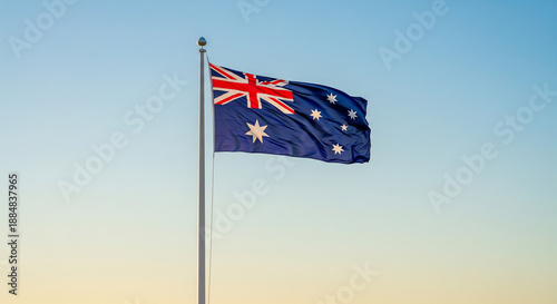 Australian flag waving on a pole against a clear blue and yellow gradient sky at sunset or sunrise