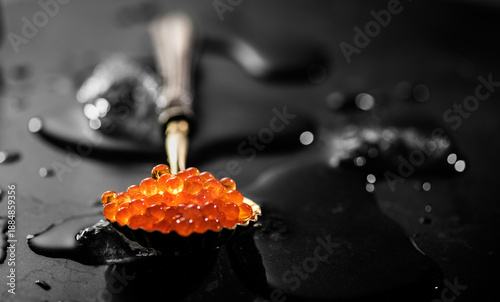 Bild auf Leinwand Red caviar in a spoon over black stone background, with ice