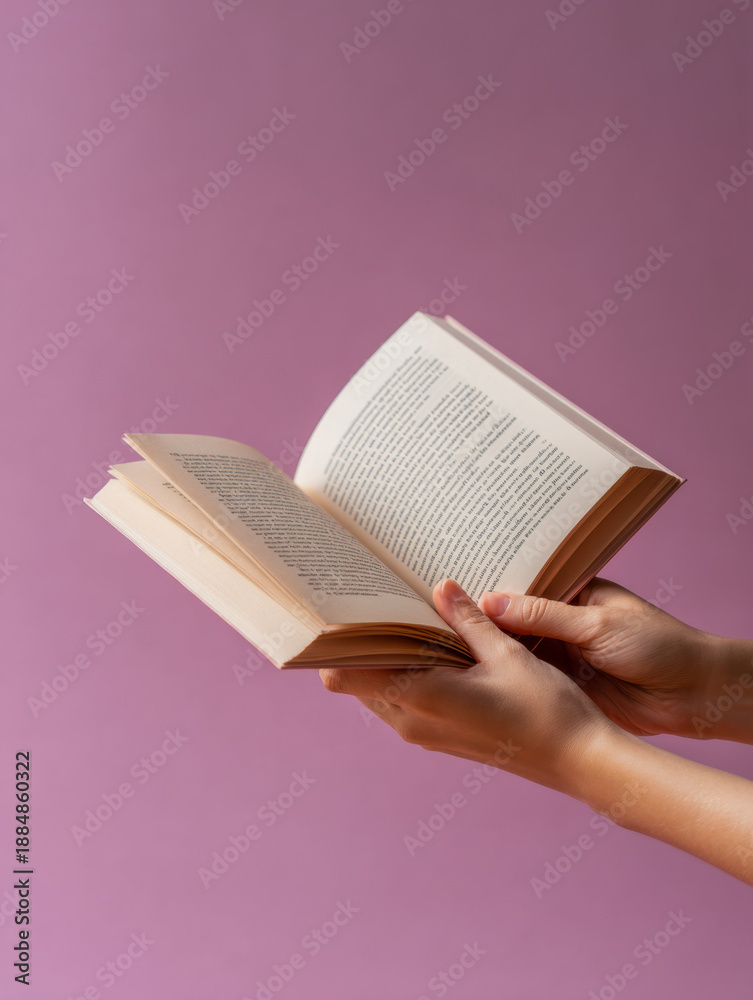 Fototapeta premium Hands holding an open paperback book with text on faded mauve background suitable for education themed or literary stock photography purposes