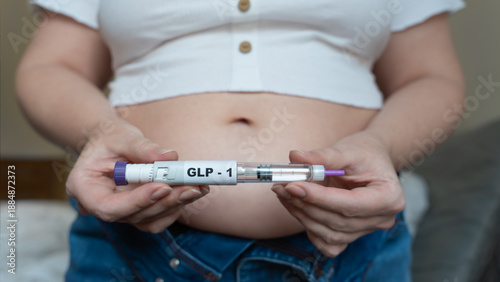 GLP-1 injection pen held by woman in front of abdomen, weight management concept