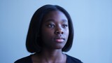 Young black woman with a calm and thoughtful expression looking away, posing against a blue studio background