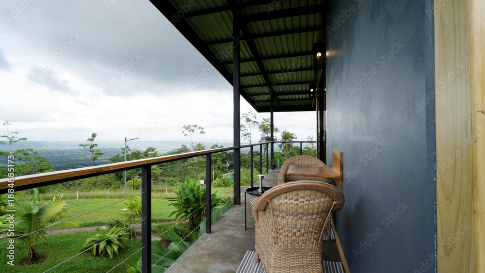 Fototapeta premium Eco friendly lodge balcony offering a relaxing view of the lush tropical jungle and valley landscape under cloudy skies in costa rica