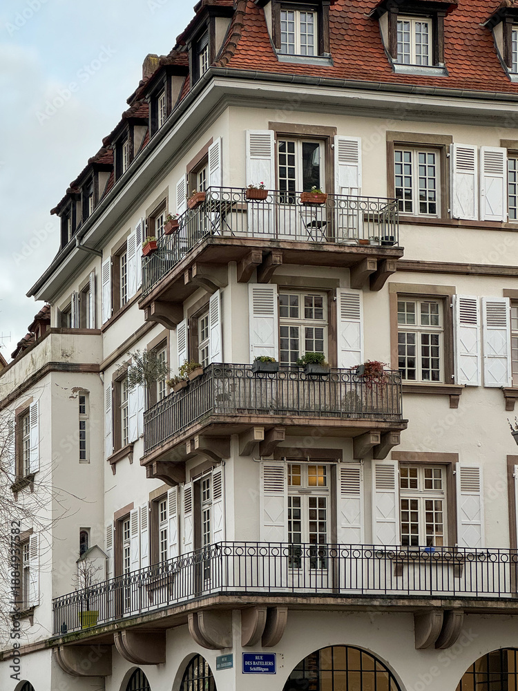 Naklejka premium Strasbourg, France – December 15, 2024. Elegant European residential building with white facade, classic balconies and shutters, traditional architecture and urban lifestyle atmosphere.