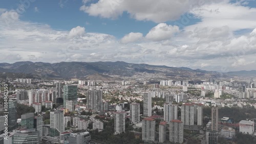 erial panoramic view of the Santa Fe district in Mexico City as the drone moves laterally over residential towers with mountains and a dramatic cloudy sky in the background.