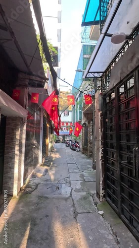 POV walking through a quiet Hanoi alley with Vietnamese flags under gentle morning light.