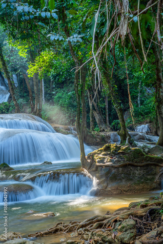 Vertical landscape of a tiered limestone waterfall illuminated by beautiful morning sun rays in a lush tropical forest. Magical nature scenery with silk water flow and dreamy light beams.