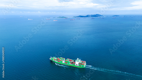 a green cargo container ship sailing in a vast blue ocean. The horizon features a busy shipping lane with many distant vessels anchored near islands. Global trade traffic and logistics concept.