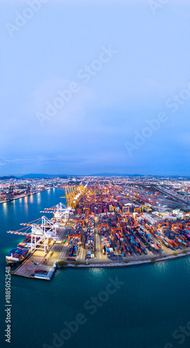 a busy deep-water cargo container port terminal during the twilight blue hour. Logistics center illuminated by industrial lights with gantry cranes and shipping vessels. Global trade infrastructure.