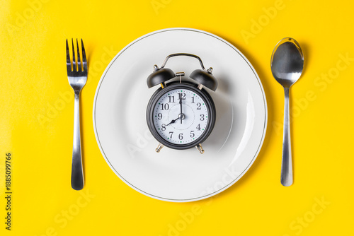 Obraz na plátně Empty plate with clock on a yellow background, intermittent fasting concept
