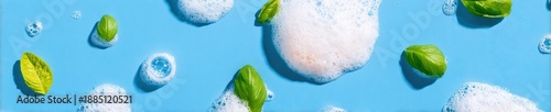 Soap foam bubbles and fresh basil leaves on a blue background creating an abstract texture for natural beauty skincare and hygiene product marketing copy space