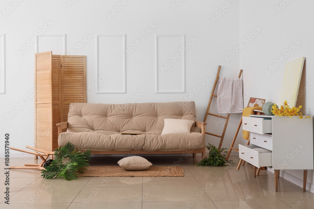 Obraz premium Interior of messy living room with white sofa and overturned furniture after earthquake