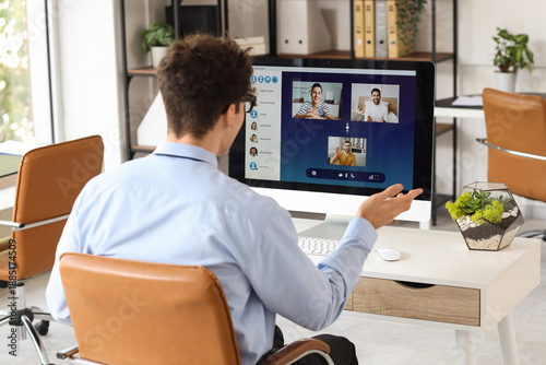 Young businessman with computer video chatting in office, back view