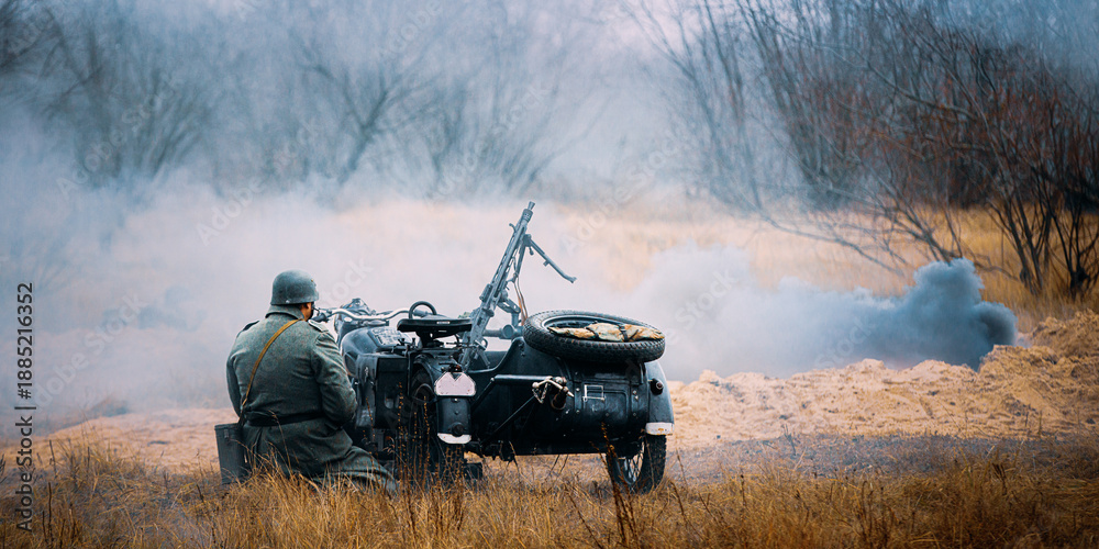 Fototapeta premium Re-enactor Dressed As World War Ii German Wehrmacht Infantry Soldier Sit Near Old Tricar, Armed Machinegun. Smokescreen. Army Three-wheeled Motorcycle In Autumn Field. Battlefield