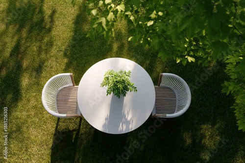 Overhead view of a round table with chairs and a plant on a sunny garden lawn with lush greenery surrounding the furniture