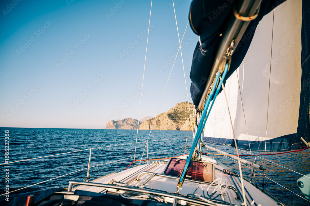 Fototapeta premium Sailboat Approaching Rocky Coastline Under Clear Skies