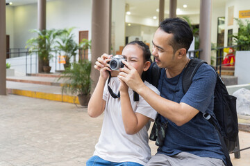 Father teaches his daughter how to use a camera, teaching her how to take photos with a digital camera during a walk at the zoo, capturing meaningful moments they share together