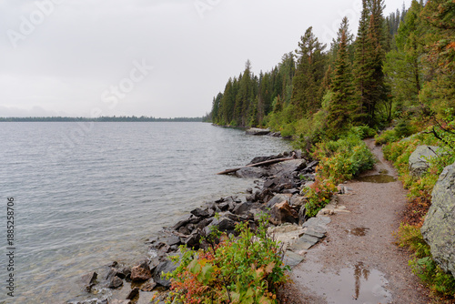 Foto Wet hiking trail along the rocky shoreline of Jenny Lake on a cloudy day, Grand