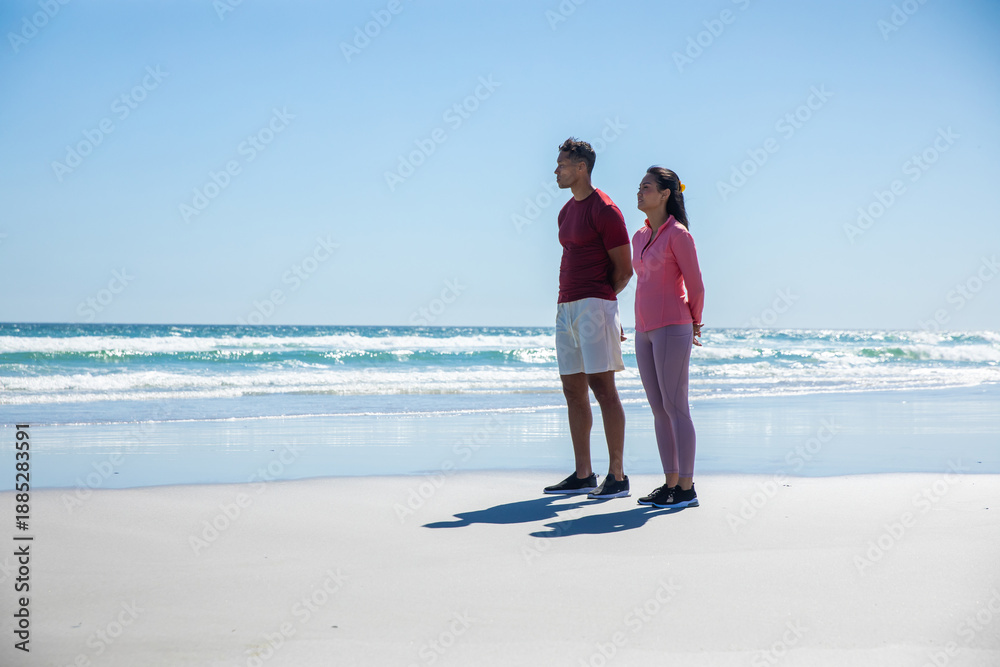 Fototapeta premium Diverse couple standing on beach facing ocean in black athletic shoes, copy space