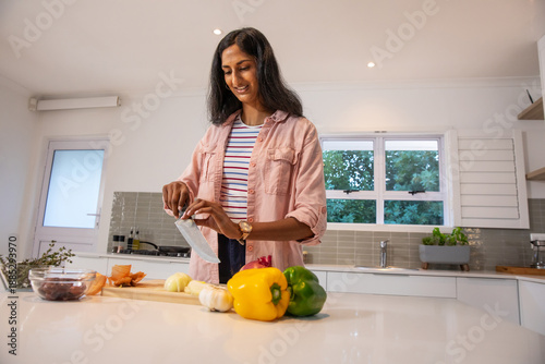 Indian woman chopping vegetables on wooden cutting board at kitchen island with peppers, olives