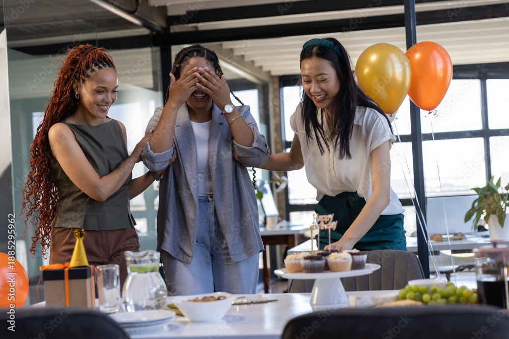 Fototapeta premium Diverse coworkers guiding surprised colleague toward cupcake stand at modern office celebration