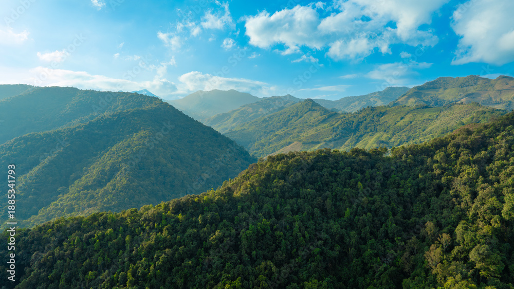 Fototapeta premium Breathtaking aerial view of lush green tropical mountains under a clear blue sky with white clouds, scenic nature landscape and eco-tourism adventure concept from drone.concept nature